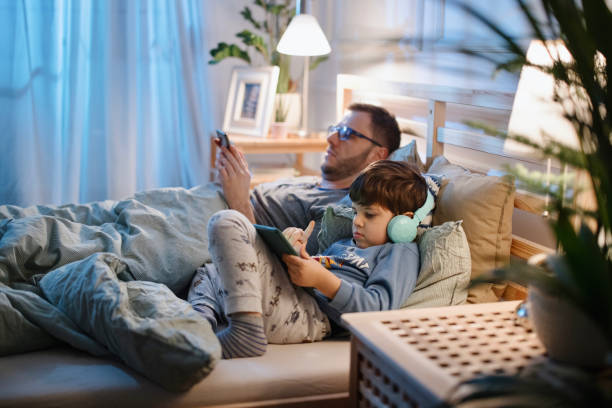 istock Little boy using digital tablet in bed at night while his father is using smartphone 1367240456