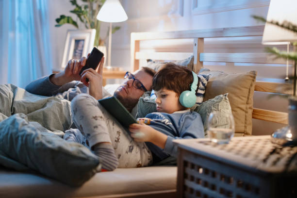 istock Little boy using digital tablet in bed at night while his father is using smartphone 1367240467