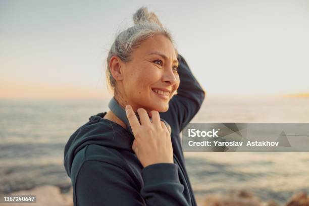 Charming Sportswoman Holding Headphones Standing By The Sea Stock Photo - Download Image Now