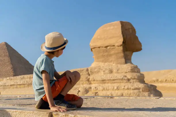 Photo of The boy in hat sits in front of the sphinx and looks at it