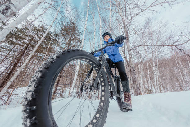 Fat bike in winter. Fat biker riding bicycle in the snow in winter. Close up action shot of fat tire bike wheels in the snow. Woman living healthy winter sports lifestyle stock photo