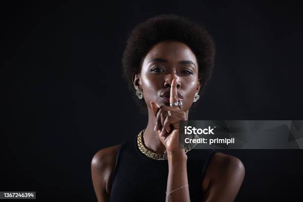 Closeup Of Beautiful Young Darkskinned Woman With Finger On Her Lips Showing Shhh Silence Gesture On Black Background Stock Photo - Download Image Now