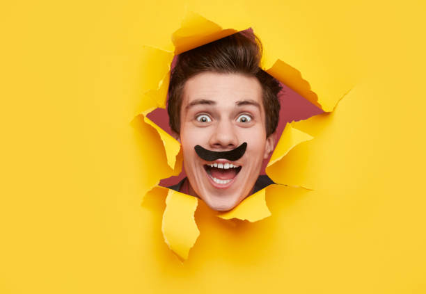 istock Funny man with mustache looking through torn paper hole 1367247167