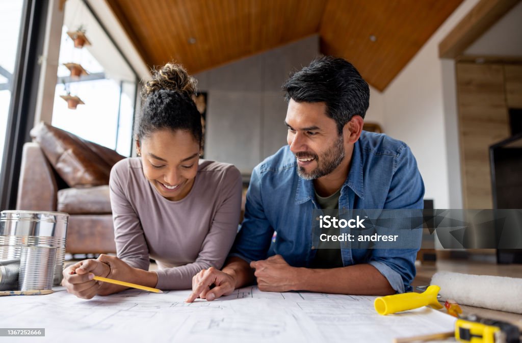 Couple remodeling their house and looking at  blueprints Happy couple remodeling their house and looking at blueprints while talking about the design - home improvement concepts. **DESIGN ON BLUEPRINT WAS MADE FROM SCRATCH BY US** Renovation Stock Photo
