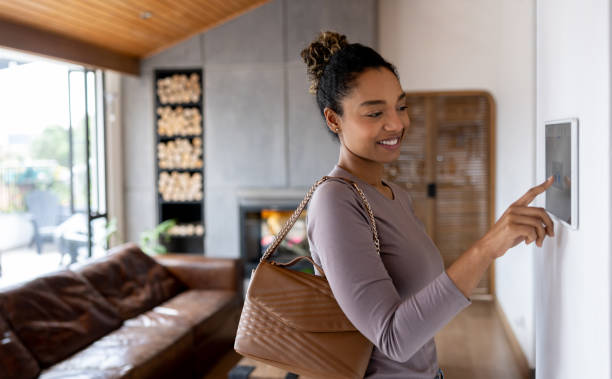 Woman activating the alarm while leaving her smart home Happy African American woman activating the alarm while leaving her smart home using an automated system. **DESIGN ON SCREEN WAS MADE FROM SCRATCH BY US** home automation stock pictures, royalty-free photos & images