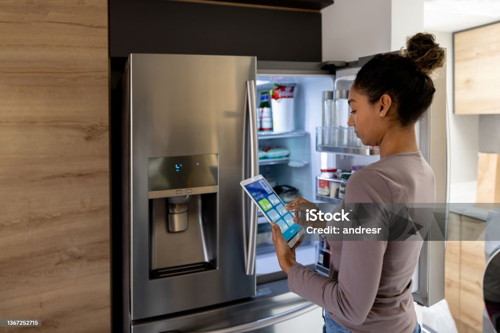 Woman controlling the fridge using an automated system from a tablet Woman controlling the fridge using an automated system from a tablet - smart home concepts. **DESIGN ON SCREEN WAS MADE FROM SCRATCH BY US** Refrigerator Stock Photo