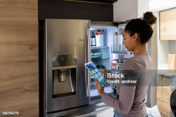 Woman Controlling The Fridge Using An Automated System From A Tablet Stock Photo - Download Image Now