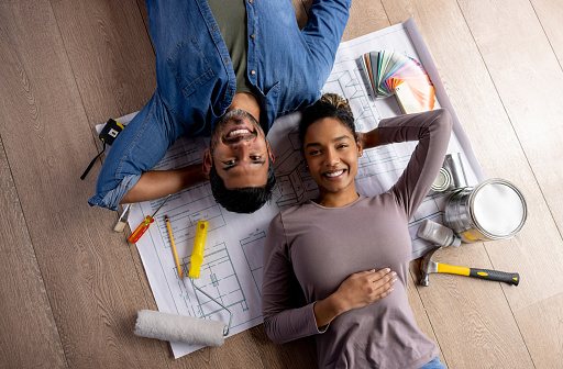 Couple working on a home addition project at their house and lying down on the floor with tools and a blueprint around them. **DESIGN ON BLUEPRINT WAS MADE FROM SCRATCH BY US**