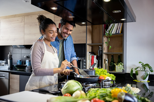 Happy Latin American couple cooking dinner together at home and smiling