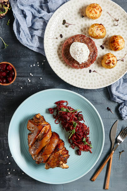 istock Composition from main courses: beefsteak with egg and roasted baby potatoes,  ham hock and braised sauerkraut. Meat menu concept. Dishes from beef and pork. Beefsteak and schweinshaxe on stone table. 1367256365