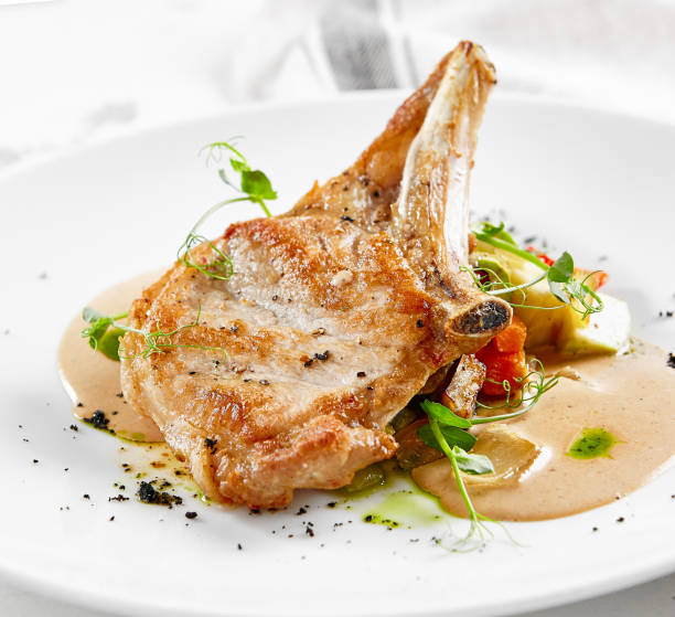 Roasted pork steak with vegetables garnish and sauce. Bone-in ribeye pork chops. Main course of pork in rustic style.