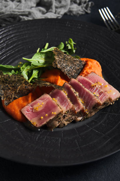 thunfischsteak mit tomatensalsa, spinat und nori auf schwarzem teller. leckeres fischgericht aus thunfischscheibenförmig auf tomatensauce im dunklen stil. moderne speisekarte. hauptgericht des fisches. - raw tuna steak marinated sauces stock-fotos und bilder