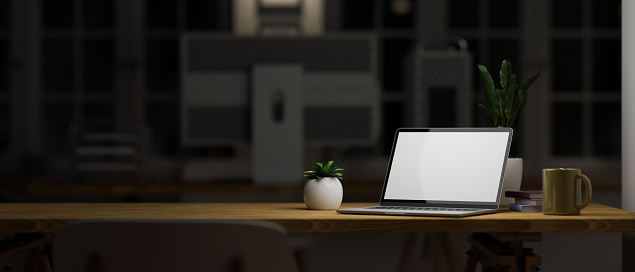 Modern dark office workstation at night concept with laptop computer mockup and copy space on wooden table under light over blurred dark office background. 3d rendering, 3d illustration