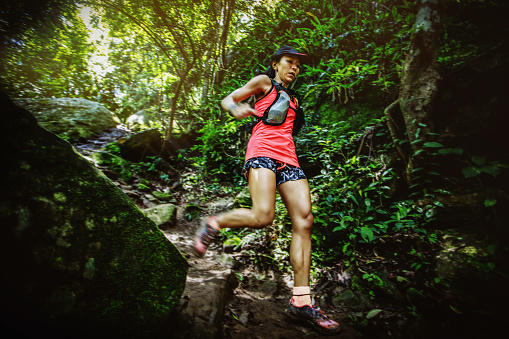 Woman ultra trail marathon runner running downhill through the tropical rainforest
