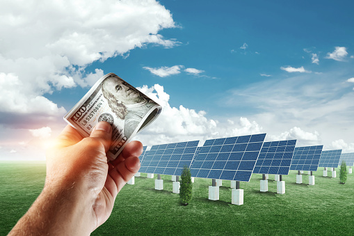 Hand with dollars on the background of solar panels.. Solar panel cost, solar powered business. The cost of green electricity, the energy of the future