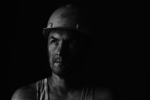 Dirty coal miner in a yellow hard hat on a dark background in a black and white photo