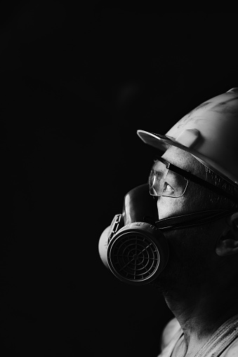 Profile portrait miner in helmet, respirator and goggles, looking at light.Dirty worker in shirt