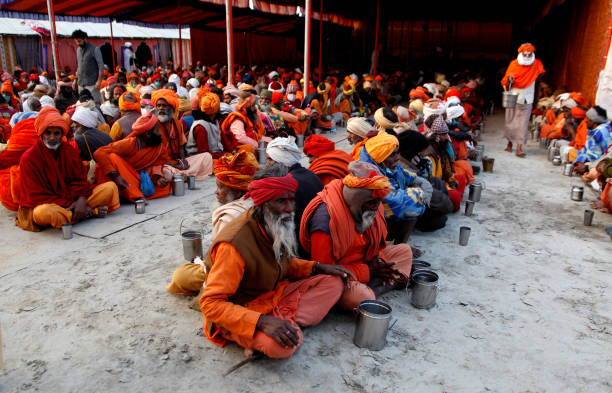 Indian Hindu devotees wearing face mask  wait for free meal at a religious camp during the Magh mela 2022 at the bank of Sangam  in Prayagraj, India. Snagam is confluence of Holy rivers Ganges, Yamuna and mythical Saraswati.  Every year around two month long Magh Mela take place at the bank of Sangam in Prayagraj, India.