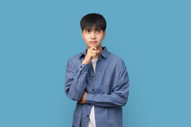 Portrait of young handsome Asian man think thoughts and  looking sideways with copy space standing on blue background. stock photo