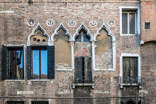 An exterior view of glass windows of an old building with metal shutters in daylight in Italy