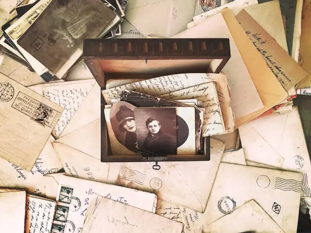 Vintage photographs and letters inside an old wooden box, surrounded by vintage post mail and photographs. High-view-angle image of photographs and letters from the beginning of the 20th century.