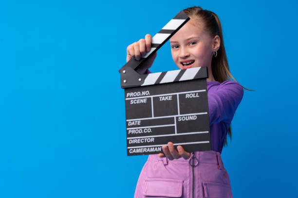 istock Smiling girl holding clapper board against blue background 1367286186
