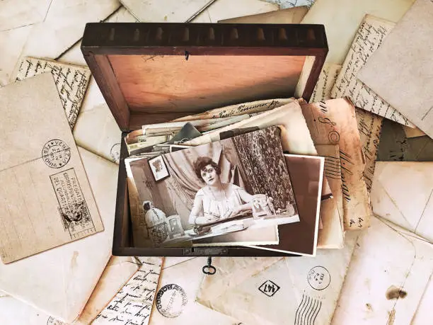 Vintage photographs and letters inside an old wooden box, surrounded by vintage post mail. High-view-angle image of photographs and letters from the beginning of the 20th century.