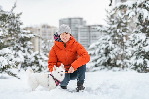 A portrait of a young woman with her dog in public park in nature in snow.