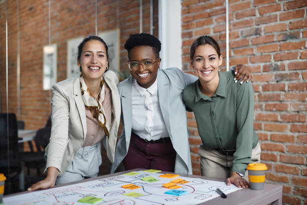 They are bold and courageous in business opportunities! Multiracial team of happy businesswomen embracing while working on new project in the office and looking at camera. mind map photos stock pictures, royalty-free photos & images