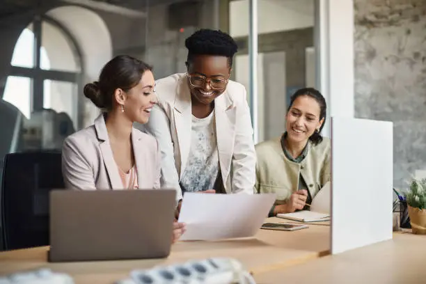 Team of happy businesswomen going through paperwork on a meeting in the office. Focus is on African American businesswoman.