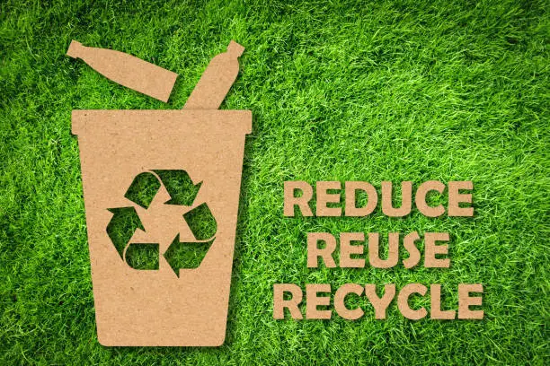 Photo of Kraft paper cut of Reuse, Reduce, Recycle symbol and text on green grass background. Environmental conservation concept.