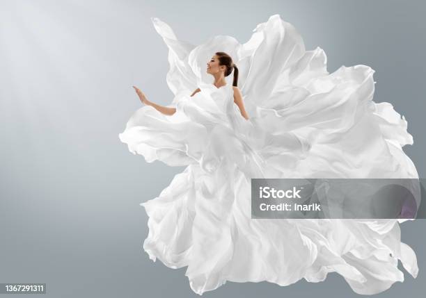 Fashion Model In Creative Pure White Dress As Cloud Woman In Long Silk Gown With Chiffon Fabric Flying On Wind Over Light Gray Background Art Fantasy Dancing Girl Stock Photo - Download Image Now