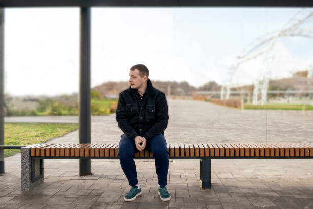 man sitting on bus stop and waiting for public transport stock photo