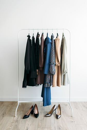Capsule of casual clothes in dark colors a rack over white background with shoes on a wooden floor