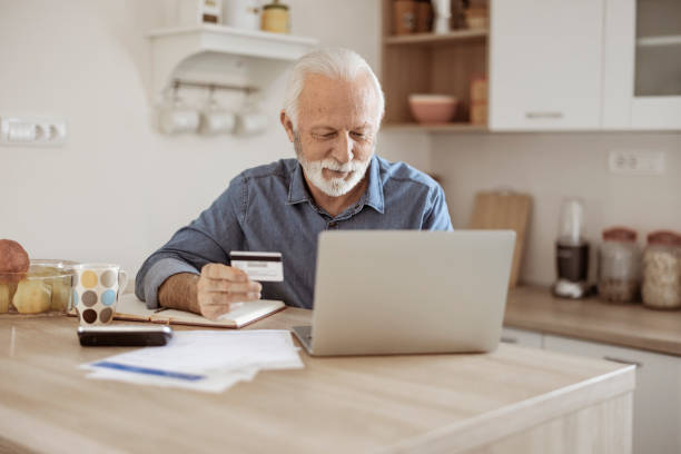 istock Senior Man Using Laptop and Holding Credit Card at Home 1367292879