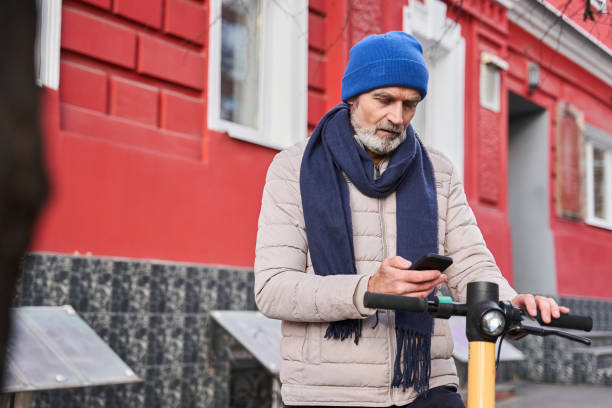 istock Millennial senior caucasian man using smartphone to unlocking urban kick scooter 1367306445