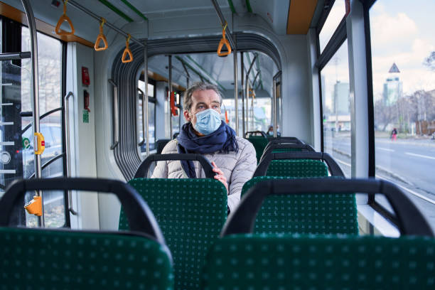 istock Grey haired man sitting at the transport and keeping protective mask at his face 1367306512
