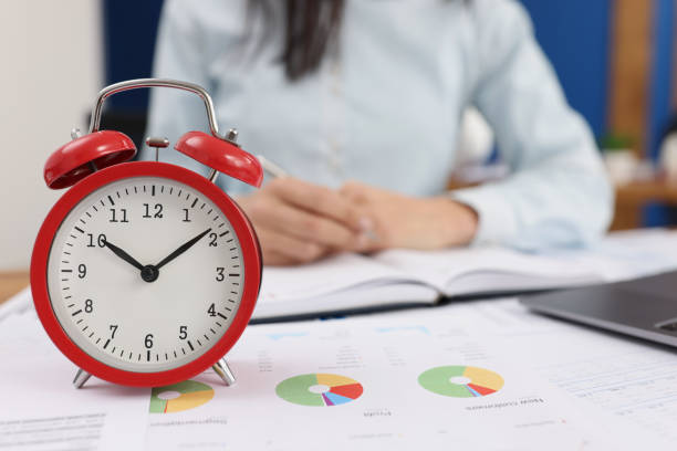 istock Red alarm clock on documents in the office, woman is blurry 1367309315