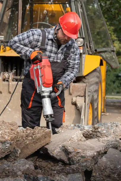 A laborer as he uses a jackhammer to break up a reinforced concrete pavement
