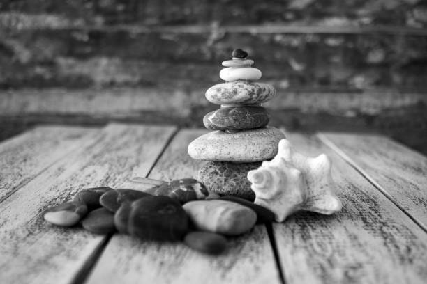 A tower of 5 pebbles stacked on top of one another symbolising balance, work life balance, about to collapse, tittering, balancing, lack of stability in grey, black and white photo