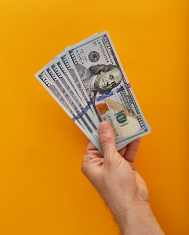 Hand holding a stack of  American One Hundred Dollar Bills over yellow / orange background