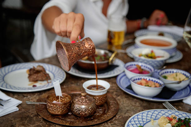 Pouring coffee from copper pot in cup, traditional in Middle Eastern culture Pouring black coffee from copper pot into cup, traditional crockery in Middle Eastern culture with specialties served on the table turkish coffee pot cezve stock pictures, royalty-free photos & images