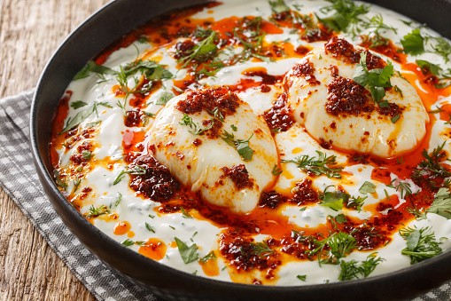 Turkish eggs or Cilbir are made with Greek yoghurt combined with fresh herbs and garlic closeup in the plate on the wooden table. Horizontal