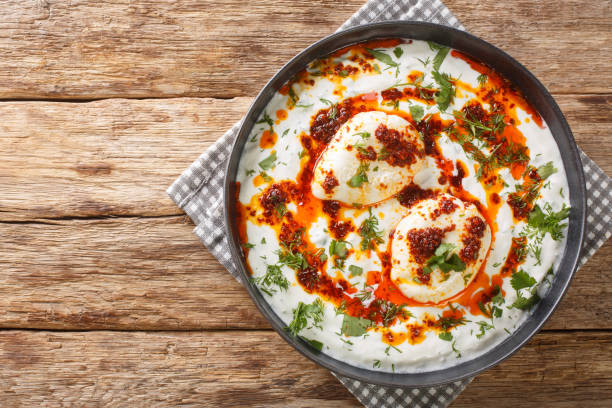 Cilbir is a Turkish eggs containing garlicky yogurt, poached eggs, and spiced melted butter in the plate. Horizontal top view Cilbir is a Turkish eggs containing garlicky yogurt, poached eggs, and spiced melted butter in the plate on the wooden table. Horizontal top view from above turkish culture stock pictures, royalty-free photos & images