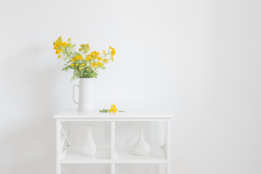 yellow wild summer flowers in jug on white vintage interior