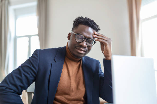 istock Head shot stressed young african american man touching forehead, suffering from terrible headache, working on computer at home office. Frustrated confused biracial guy having painful feelings in head. 1367320603