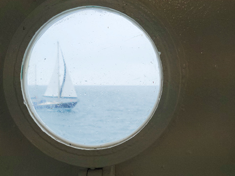 A single yacht viewed through a ferry port hole at dawn in Penzance harbour, Cornwall, UK.