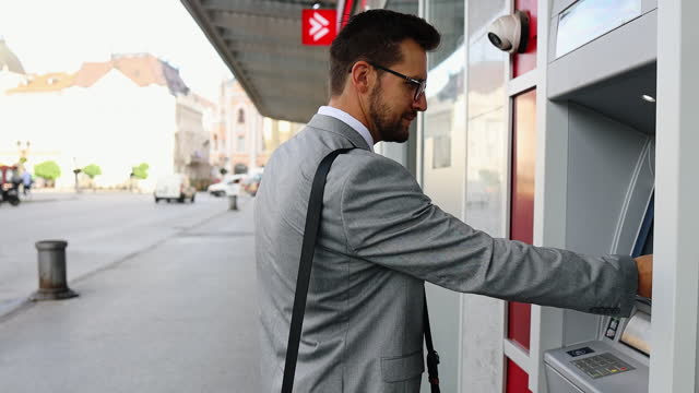 Businessman on city street using ATM machine
