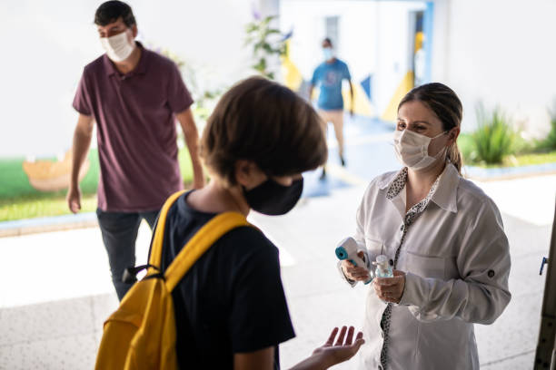 istock Teacher applying hand sanitizer on a student's hand before entering school - using a face mask 1367323745