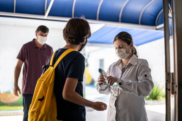 istock Teacher applying hand sanitizer on a student's hand before entering school - using a face mask 1367323751